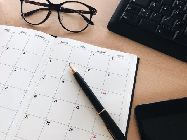 机に置かれた手帳のカレンダーとペン、眼鏡